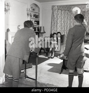 Années 1950, la photographie amateur... deux collégiens de prendre une photo avec un appareil-photo de film Kodak Brownie d'une femme assise avec un enfant sur une chaise à l'intérieur d'une salle de séjour. L'un des garçons d'Othe est titulaire d'une lampe de poche, tandis que le garçon en photo utilise une table comme un trépied de fortune, England, UK. Banque D'Images