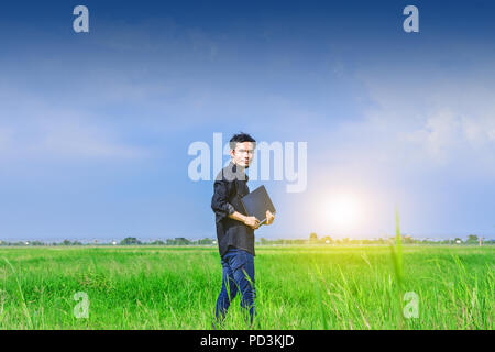 Man holding computer in green field under blue sky.Blogger Ciel et nuages Banque D'Images