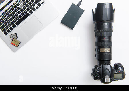 Vue du haut vers le bas de l'équipement de l'appareil photo sur la table blanche, reflex numérique avec zoom téléobjectif, cartes mémoire et macbook Banque D'Images