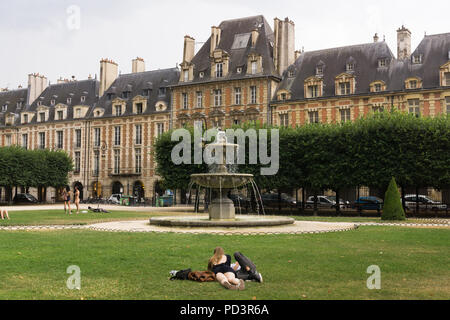 Place des Vosges Paris - Couple relaxing on grass à Place des Vosges dans le quartier du Marais de Paris, France, Europe. Banque D'Images