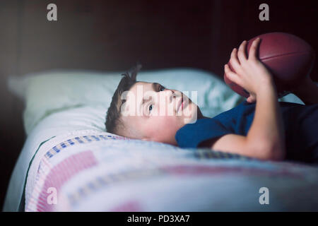 Garçon sur le lit avec le football américain Banque D'Images