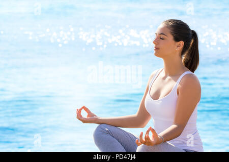 Close up portrait of young woman in yoga position à l'extérieur. Girl in wear assis contre la mer bleue avec fond réfléchissant sur Sun Banque D'Images
