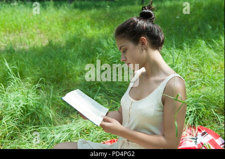 Une fille est assise sur l'herbe et lit un livre Banque D'Images