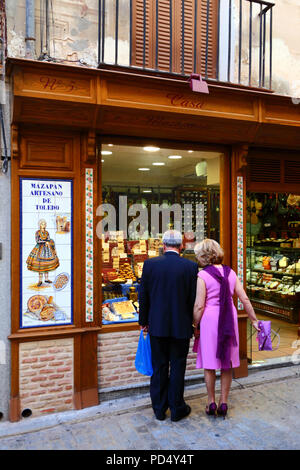 Mari et femme bien habillés regardant par la fenêtre du magasin vendant le célèbre massepain local, Tolède, Castille-la Manche, Espagne Banque D'Images