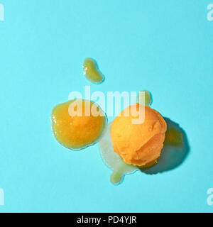 Cuillère à crème glacée de jaune et la crème glacée fondue sur un fond bleu avec des ombres Banque D'Images