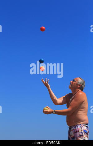 Jongleur de rue avec quatre boules colorées sur fond de ciel bleu Banque D'Images