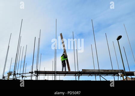 Silhouette of construction worker holding wooden board sur le dessus des nouveaux aménagements de la baie entourée de poteaux métalliques contre le ciel bleu Banque D'Images