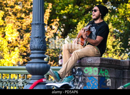 Musicien de rue jouant de la guitare sur un pont à Kreuzberg, Berlin, entouré de graffitis et de couleurs d'automne, créant une ambiance urbaine décontractée. Banque D'Images