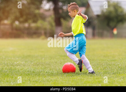 Boy kicking football sur le terrain de sport au cours de match de football Banque D'Images