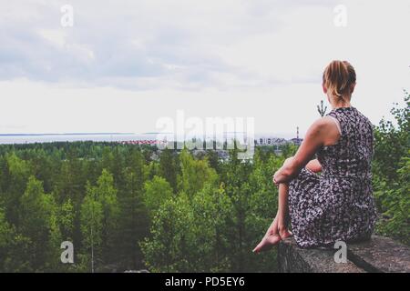 Une jeune fille dans une robe se situe sur une saillie rocheuse au-dessus de la forêt, qui est situé sur le bord d'un immense lac. À partir de la hauteur vous pouvez voir les chambres spacieuses Banque D'Images