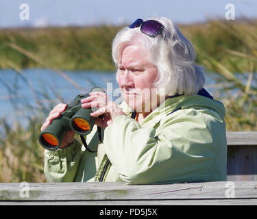 Une femme aux cheveux d'argent avec des jumelles de vue de la faune à l'Leonabelle Turnbull Birding Center à Port Aransas, Texas USA. Banque D'Images