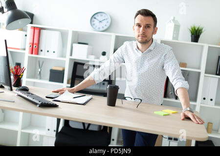 Un jeune homme se tient dans le bureau près de la table, posant ses mains sur lui. Banque D'Images