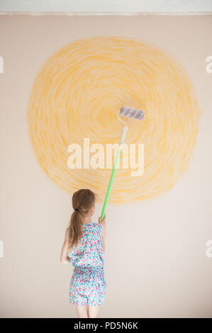 Mince petit caucasian girl painting soleil sur wall with paint roller Banque D'Images