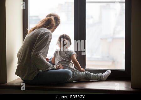 Vue arrière à kid fille et mère assis sur sill Banque D'Images