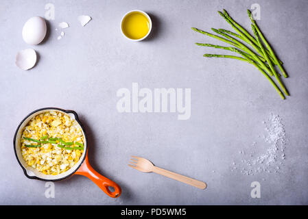 Le petit-déjeuner fraîchement préparé, œufs frits dans un plat de cuisson avec des asperges fraîches. Mise à plat, vue du dessus. Banque D'Images