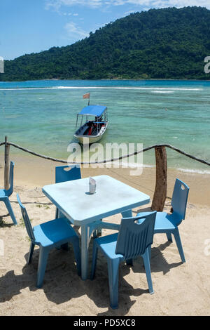 Table en plastique bleu et quatre chaises en plastique bleu sur une plage jetée avec la plage de vitesse et un petit bateau ancré près de la plage, mer bleue et verte tre Banque D'Images