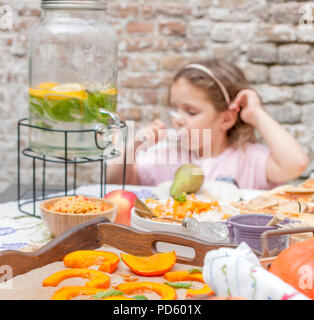 Une petite fille mange une tarte et boit de la limonade. Dîner familial dans la cour extérieure. Légumes et fruits d'automne sur la table. Table de dîner . Un lieu spécial pour le texte Banque D'Images