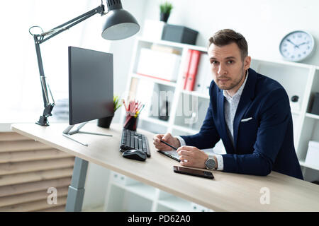 Un jeune homme se tient près d'une table dans l'office, est titulaire d'un crayon dans sa main et fonctionne avec les documents et un ordinateur. Banque D'Images