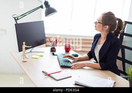 Une jeune fille est assise à une table, tenant un crayon dans sa main et le travail à l'ordinateur. Banque D'Images