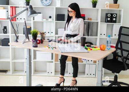 Une jeune fille se tient près d'une table et s'imprime sur le clavier. Avant de la fille est un tableau magnétique et marqueurs. Banque D'Images