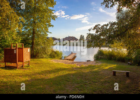 Plage par un lac ou une rivière sur un soir au coucher du soleil avec un banc en bois, dressing et pier Banque D'Images