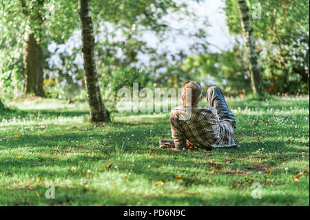 Jour d'été de détente dans un parc, les gens se prélasser sur l'herbe, l'eau de bassin en arrière-plan. Concept de hygge. Banque D'Images