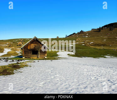 Vieux bois cabane dans un paysage vallonné avec de la neige sur l'herbe sous un ciel bleu Banque D'Images