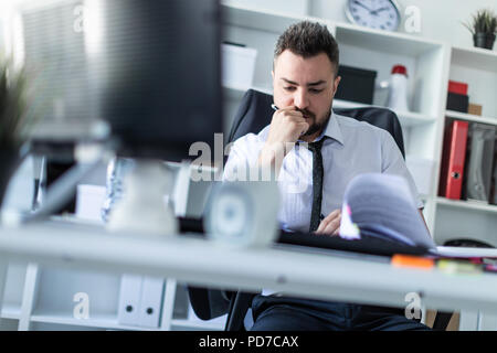 Un homme est assis dans le bureau et de faire défiler les documents. photo avec la profondeur de champ, a mis l'accent sur l'homme. Banque D'Images