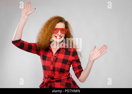 Jeune fille rousse dans une chemise à carreaux rouge. Charmante Jeune fille en rouge lunettes. Young Girl Dancing Banque D'Images