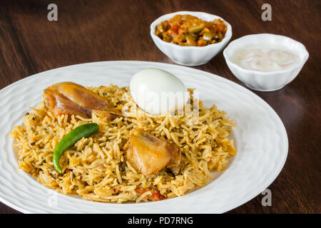 Vue rapprochée de la partie supérieure de délicieux biryani poulet indien servi avec côtés traditionnels, l'oeuf, raita et sauce. Lumière naturelle utilisée. Banque D'Images