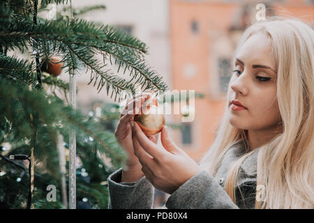 Une belle jeune femme blonde touche un arbre de Noël ou la balle jouet ou décore un arbre de Noël. Banque D'Images