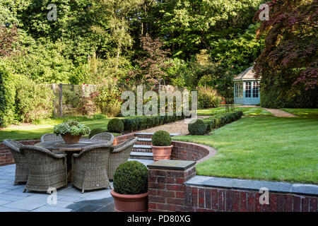 Meubles en rotin dans neat country garden avec fort haie et maison d'été Banque D'Images