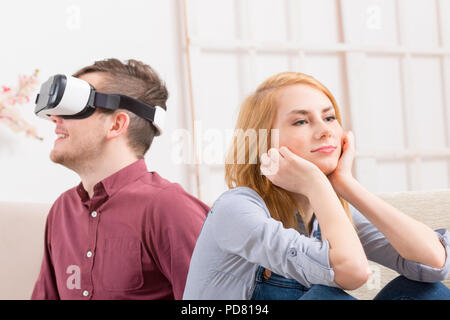 Jeune homme à l'aide de casque de réalité virtuelle et sa petite amie ou partenaire mécontents de cette situation Banque D'Images