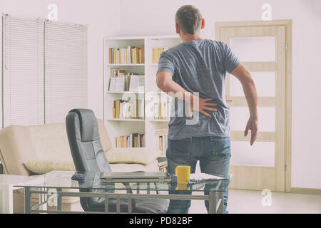 Homme de bureau à domicile qui souffrent de maux de dos, debout près de 24 avec un ordinateur portable, des documents et autres objets Banque D'Images