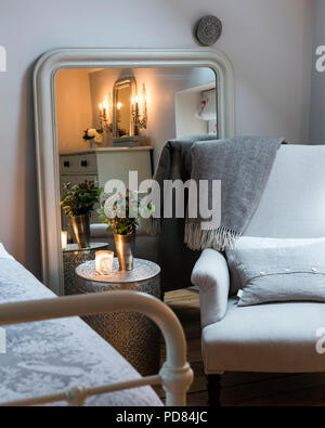 Fauteuil et couverture de laine jetez dans coin chambre avec grand miroir, fleurs fraîches et bougies Banque D'Images