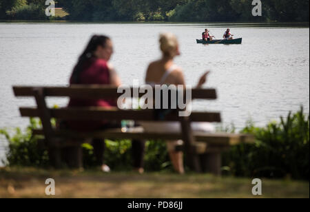 07.08.2018, Bade-Wurtemberg, Stuttgart : Deux jeunes femmes profitez de la vue sur le lac Max-Eyth dans l'ombre des arbres, tandis que deux canoéistes passent. Photo : Christoph Schmidt/dpa Banque D'Images