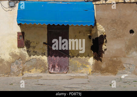 Vue d'une rue sur une porte fermée d'une boutique dans une maison ancienne. Marquise de l'ombre bleue pour certains. La peau de mouton accroché près de la porte. El Jadida, Maroc. Banque D'Images