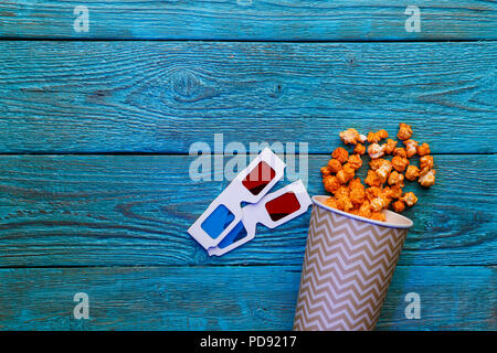 Tasse de papier avec le pop-corn et les lunettes 3D sur fond bleu. Vue d'en haut. Banque D'Images