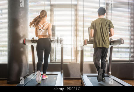 Jeune homme et femme tournant sur des tapis roulants lors de l'entraînement Banque D'Images