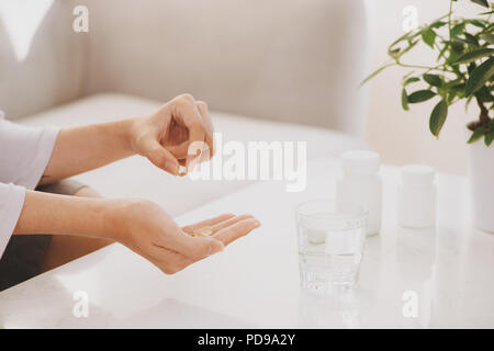 Prend la main d'oméga 3 capsules jaunes, pilules blanches de la glucosamine et du calcium sur la boîte en plastique, verre avec l'eau à la table en bois, vue du dessus. Banque D'Images