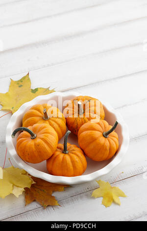 Mini citrouilles orange dans une assiette blanche sur fond de bois Banque D'Images