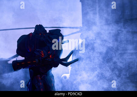 Grand robot effrayant passe près de l'hélicoptère militaire à travers les nuages de fumée en ville au centre-ville. Avoir la main énorme corpus, métallique, rouge diods rétroéclairage Banque D'Images