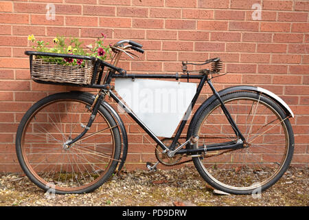 Rusty old fashioned merchant's location appuyé contre un mur de brique rouge avec prix pour copier du texte. Publicité vélo avec panier de fleurs sur le devant. Banque D'Images