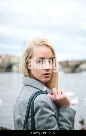 Blonde aux cheveux longs à la mode dans un manteau près de Pont Charles à Prague. Belle jeune femme à l'extérieur. Banque D'Images