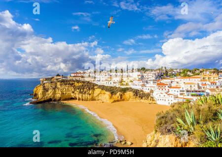 Une large plage de sable, maisons blanches, ciel nuageux avec mouettes, Carvoeiro, Algarve, Portugal Banque D'Images