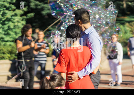 Couple jouant avec des bulles de savon arc-en-ciel géant flottant dans l'air d'été au cours d'une belle journée ensoleillée. Fun jeu amusant pour les enfants et les adultes. Banque D'Images