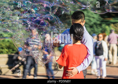 Couple jouant avec des bulles de savon arc-en-ciel géant flottant dans l'air d'été au cours d'une belle journée ensoleillée. Fun jeu amusant pour les enfants et les adultes. Banque D'Images