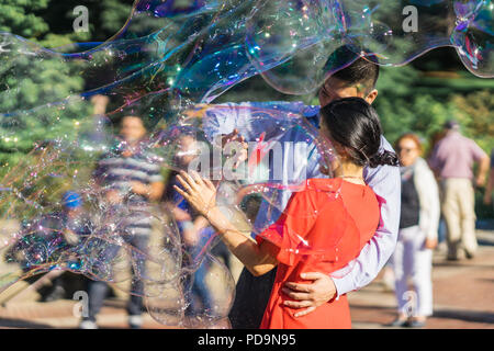 Couple jouant avec des bulles de savon arc-en-ciel géant flottant dans l'air d'été au cours d'une belle journée ensoleillée. Fun jeu amusant pour les enfants et les adultes. Banque D'Images