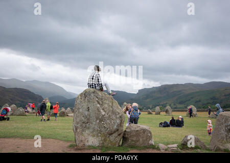 Un jeune visiteur de cercle de pierres de Castlerigg est assis sur le dessus d'un grand standing stone au cercle de pierres de Castlerigg, Cumbria, Royaume-Uni Banque D'Images