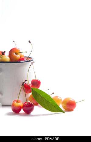 Tasse blanche avec les baies mûres de cerise douce jaune et plusieurs fruits avec feuille verte d'cherry tree sur fond blanc Banque D'Images